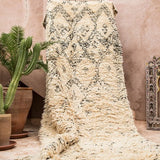A fluffy shag pile vintage Beni Ourain rug being held up in front of a soft pink wall - Nouvelle Nomad