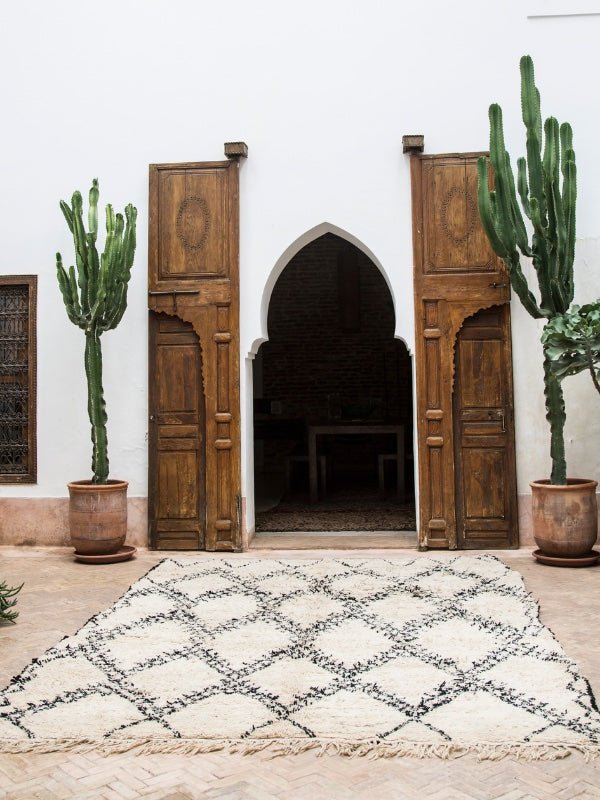 A low-pile vintage Moroccan Beni Ourain rug laying out flat on the ground in front of Moroccan doors and cactus pots - Nouvelle Nomad