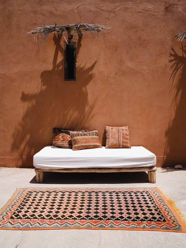 Black Moroccan rug from Taznakht on the ground with a couch and cushions in the sunshine - Nouvelle Nomad