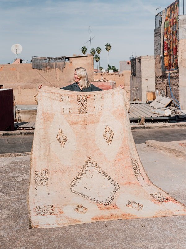 A feded pink vintage Moroccan rug being held up on a rooftop in Marrakech Morocco - Nouvelle Nomad