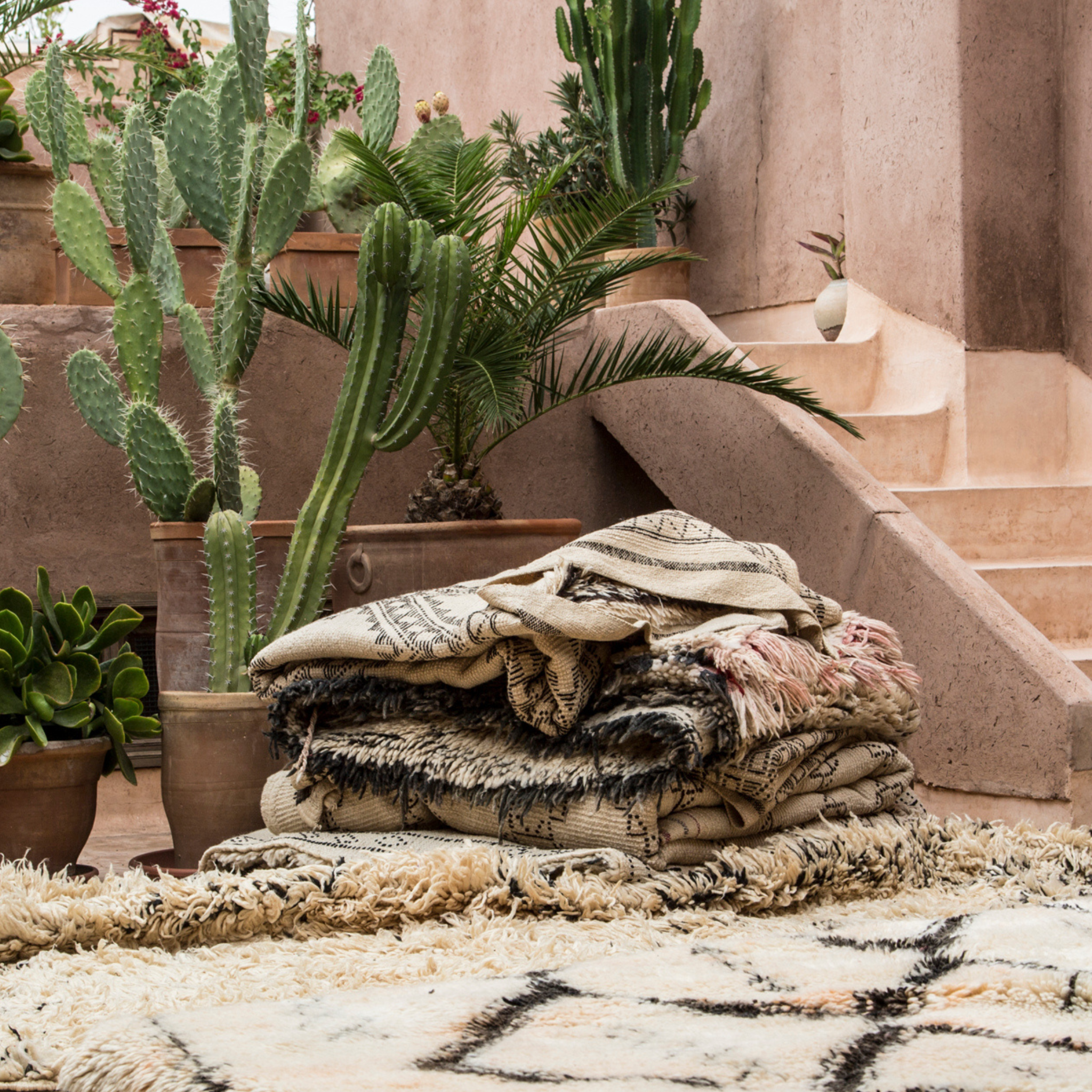 A pile of authentic vintage Beni Ourain rugs with cactus pots in the background