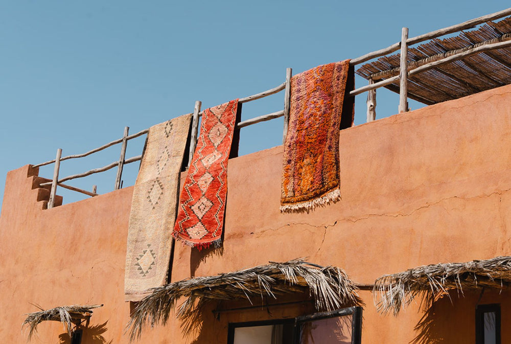 Three vintage Moroccan runners hanging over a terracotta wall in Morocco | Nouvelle Nomad
