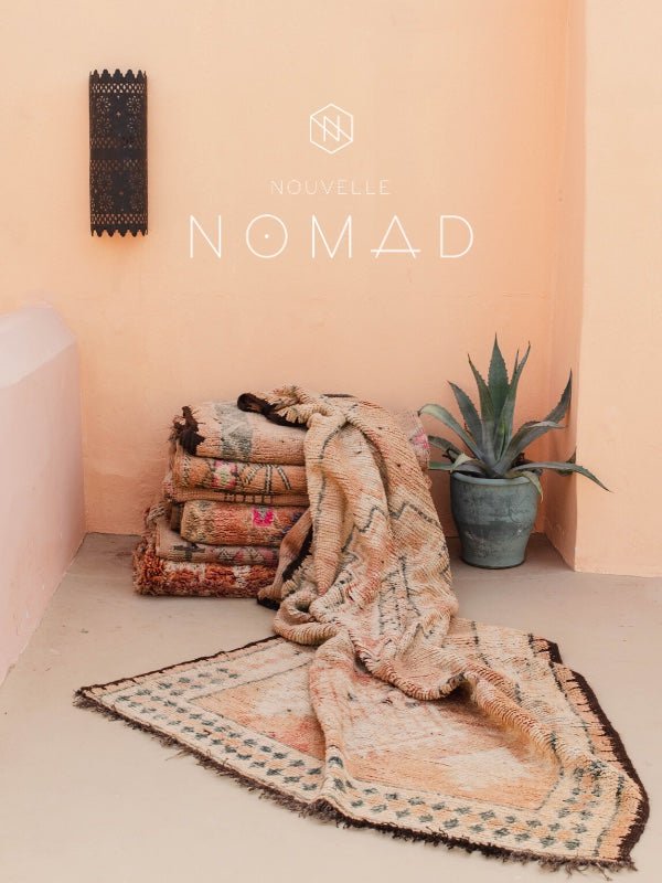A stack of peach and pink coloured vintage Moroccan rugs against a peach background - Nouvelle Nomad