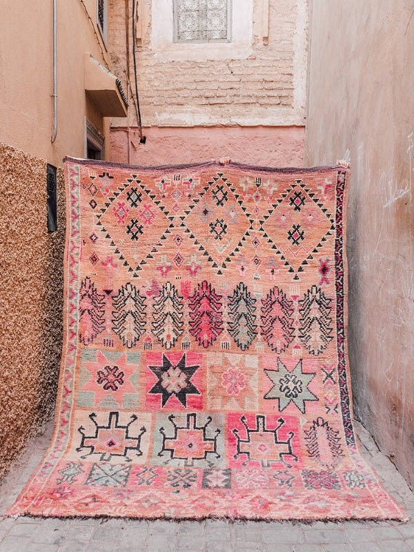 A pink vintage Moroccan Boujad rug being held up in a street in Marrakech - Nouvelle Nomad